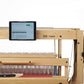 A Louët Megado Electronic Dobby Head V2.0 by Louët Inc. is set up on a white background, featuring a digital tablet displaying weaving software. The loom, equipped with metal components and a control panel, utilizes Computer Dobby technology for precise pattern creation.