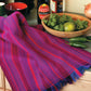 A kitchen counter showcases the vibrant "Best of Handwoven Yarn Series: A Dozen Projects in 10/2 Pearl Cotton" tablecloth by Long Thread Media, complemented by a soy sauce bottle and a wooden bowl containing cilantro, a lime, and a red onion. Nearby, green chilies add to the colorful scene, while assorted bottles and bowls enhance the inviting background.