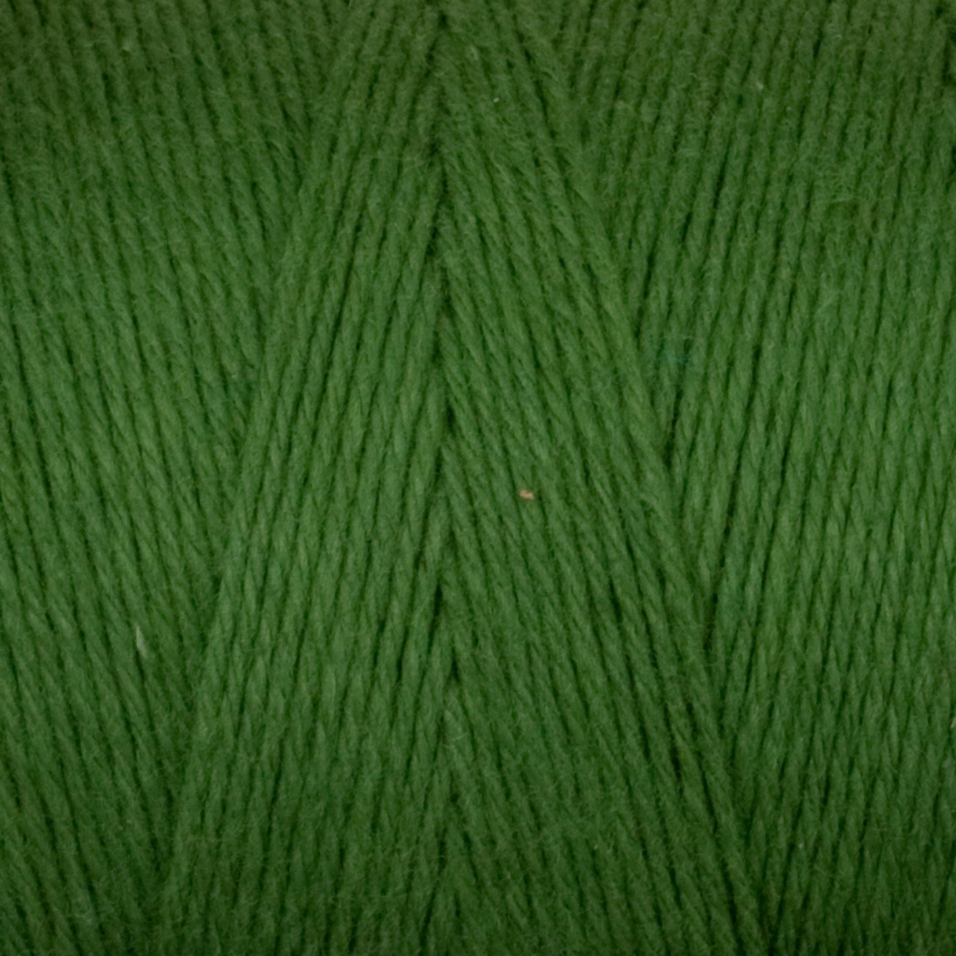 A close-up of Cotton Carpet Warp 8/4 yarn reveals tightly wound green fibers with diagonal lines, offering a soft, slightly shiny texture for a smooth finish—perfect for weaving colorfast rag rugs.