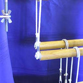 A section of a wooden Leclerc Floor Loom with purple fabric in the background. The loom features several wooden rods and strings with metal clips and bolts, likely used for tension and adjustment, along with a Leclerc White Pulley with screw from Leclerc Looms to aid in the weaving process.