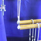 A section of a wooden Leclerc Floor Loom with purple fabric in the background. The loom features several wooden rods and strings with metal clips and bolts, likely used for tension and adjustment, along with a Leclerc White Pulley with screw from Leclerc Looms to aid in the weaving process.