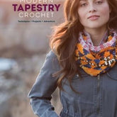 The cover of "Modern Tapestry Crochet" by Alessandra Hayden, published by Ingram Content, showcases a woman with long brown hair modeling a vibrant crocheted scarf that highlights intricate colorwork patterns. She is dressed in a gray jacket and stands against a blurred, natural background.