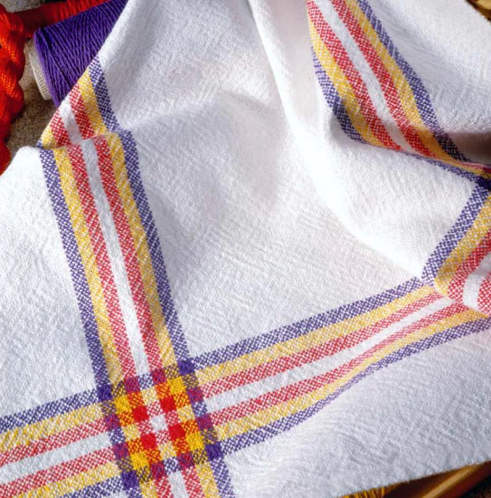 A flat white fabric boasting red, yellow, and purple striped plaid patterns lies seamlessly. A section of a red rope subtly emerges from the left side while a spool of purple thread sits gracefully in the top left corner. Ideal for crafting vibrant napkins or coordinating sets of placemats and napkins using "Best of Handwoven Yarn Series: A Dozen Projects in 8/2 Cotton" by Long Thread Media.