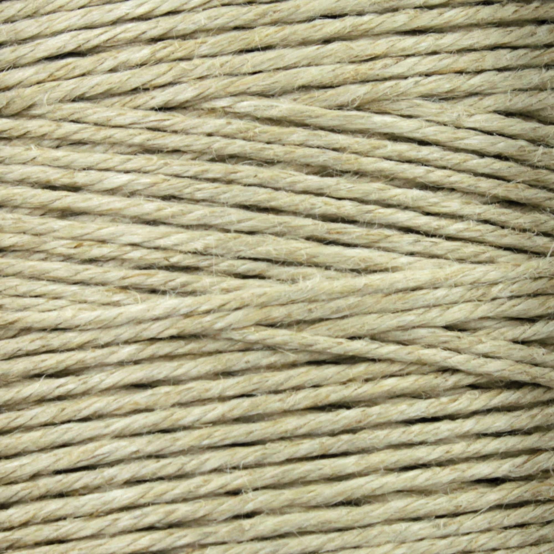 A close-up of a spool of beige twine displays tightly wound fibers, similar to Soft Finish Linen Warps used in tapestry weaving. Its coarse, natural texture and visible horizontal strands echo the craftsmanship found in Scandinavian rug creation.