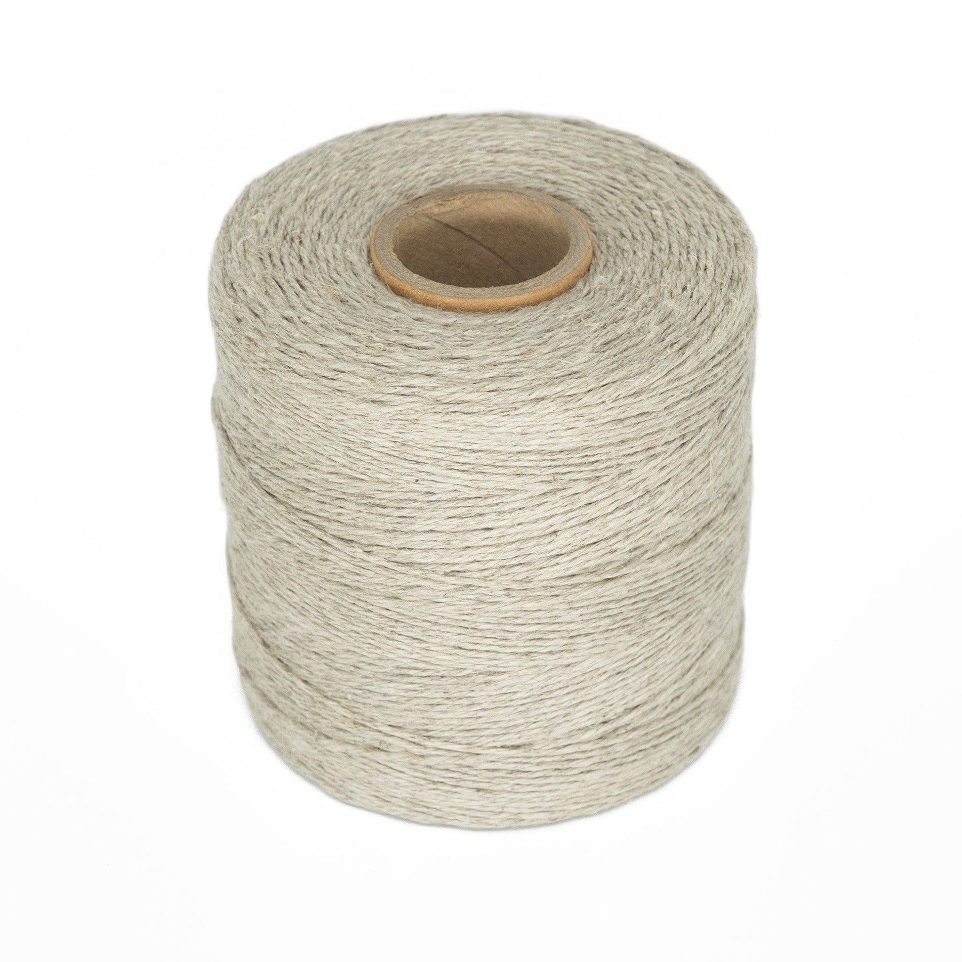 The Soft Finish Linen Warps, a spool of light gray twine with tightly wound threads ideal for tapestry weaving, stands upright on a white background. It features a visible cardboard core at the center.