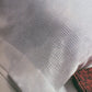 Close-up of a white pillow with a textured, checkered design similar to Swedish lace along the edge. The "Best of Handwoven New Technique Series: Atwater-Bronson Lace eBook" from Long Thread Media is partially visible at the bottom right corner, showcasing its red patterned cover.