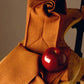 A red apple sits on a beautifully folded piece of fabric from the "Best of Handwoven Yarn Series: A Dozen Projects in 10/2 Pearl Cotton (Printed Version)" by Long Thread Media, draped over a wooden chair. The fabric, reminiscent of a fine tablecloth, features a subtle geometric pattern that adds texture to the arrangement. The background is plain, keeping the focus on the apple and the exquisite fabric.