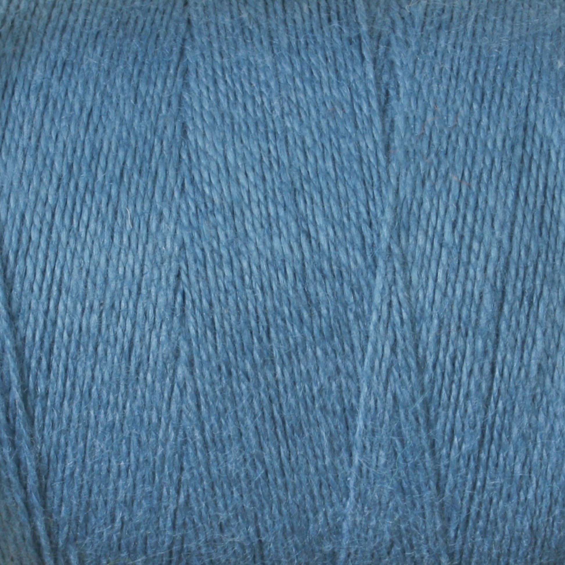 Close-up image of a spool of blue yarn. The yarn, part of the 8/2 Cottolin Organic Yarn | Tube by Maurice Brassard, is tightly wound into neat layers and has a slightly textured surface, showcasing a consistent blue color throughout.