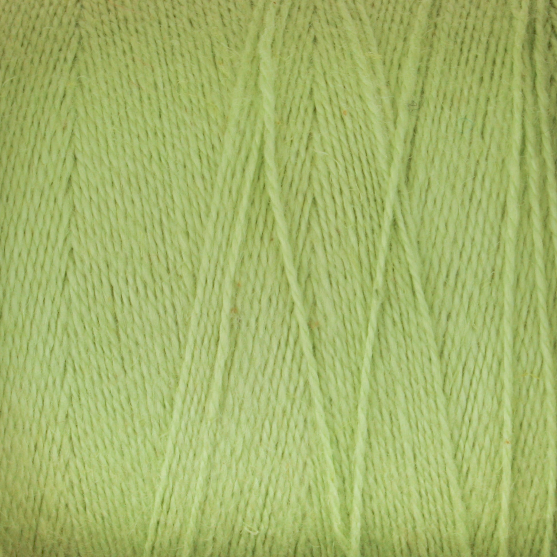 A close-up image of a spool of light green Maurice Brassard 8/2 Cottolin Organic Yarn, neatly wound in a criss-cross pattern, creating a textured and detailed view of the fibers. The color is a soft, pastel green, perfectly suited for projects like the Cottolin Tea Towel Kit.