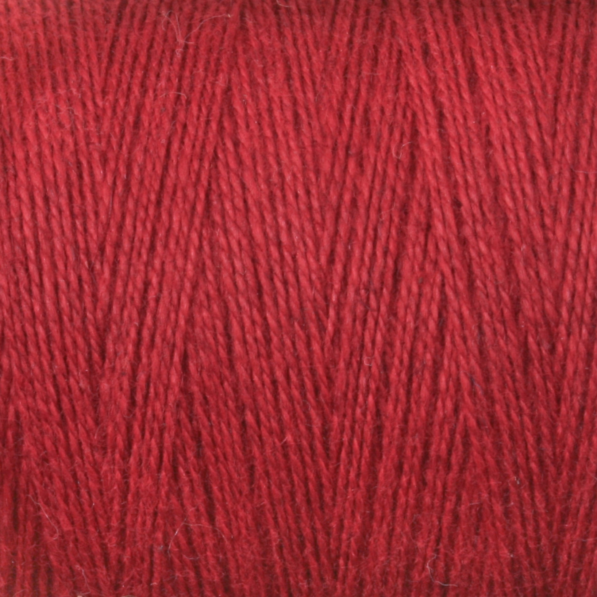 Close-up shot of tightly wound 8/2 Cottolin Organic Yarn from Maurice Brassard, showcasing its vibrant red color and soft texture. The detailed image highlights the individual strands and slight variations in the hue, with a uniform crisscross pattern reminiscent of those created on a four shaft loom.