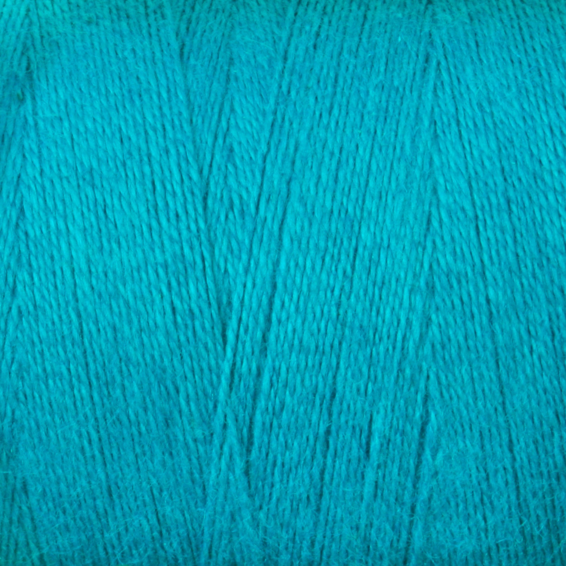 Close-up image of a spool of Maurice Brassard's 8/2 Cottolin Organic Yarn on a tube. The bright blue-green fibers are tightly wound, with a soft and slightly fuzzy texture that highlights the even thickness and appealing color—making it an ideal choice for weaving projects using a four-shaft loom.