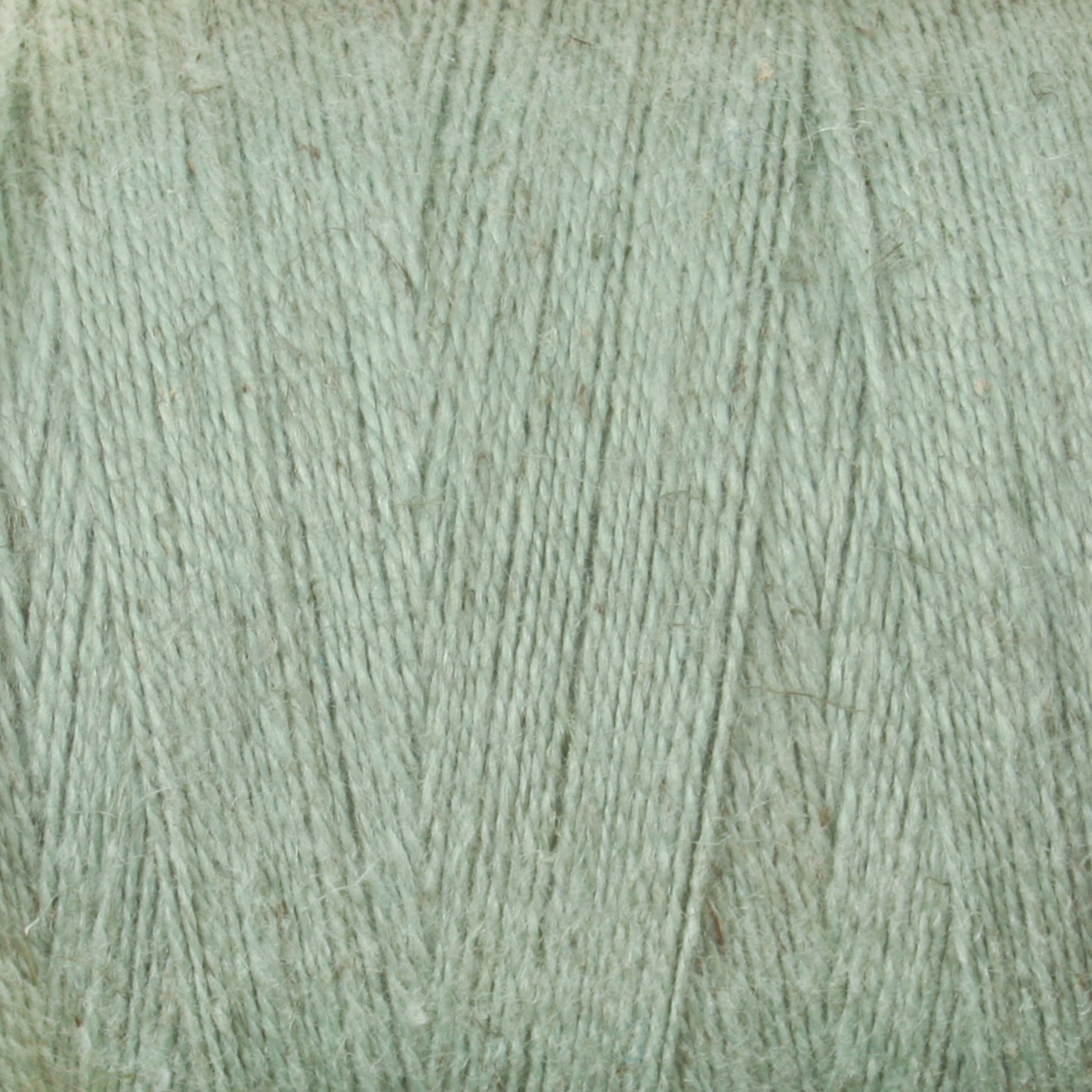 A close-up image of a spool of Maurice Brassard's 8/2 Cottolin Organic Yarn | Tube, tightly wound into a cylindrical shape. The texture of the cotton-linen blend is clearly visible, with fibers appearing soft and slightly fuzzy. The color is a pastel green, creating a calm and soothing visual effect.