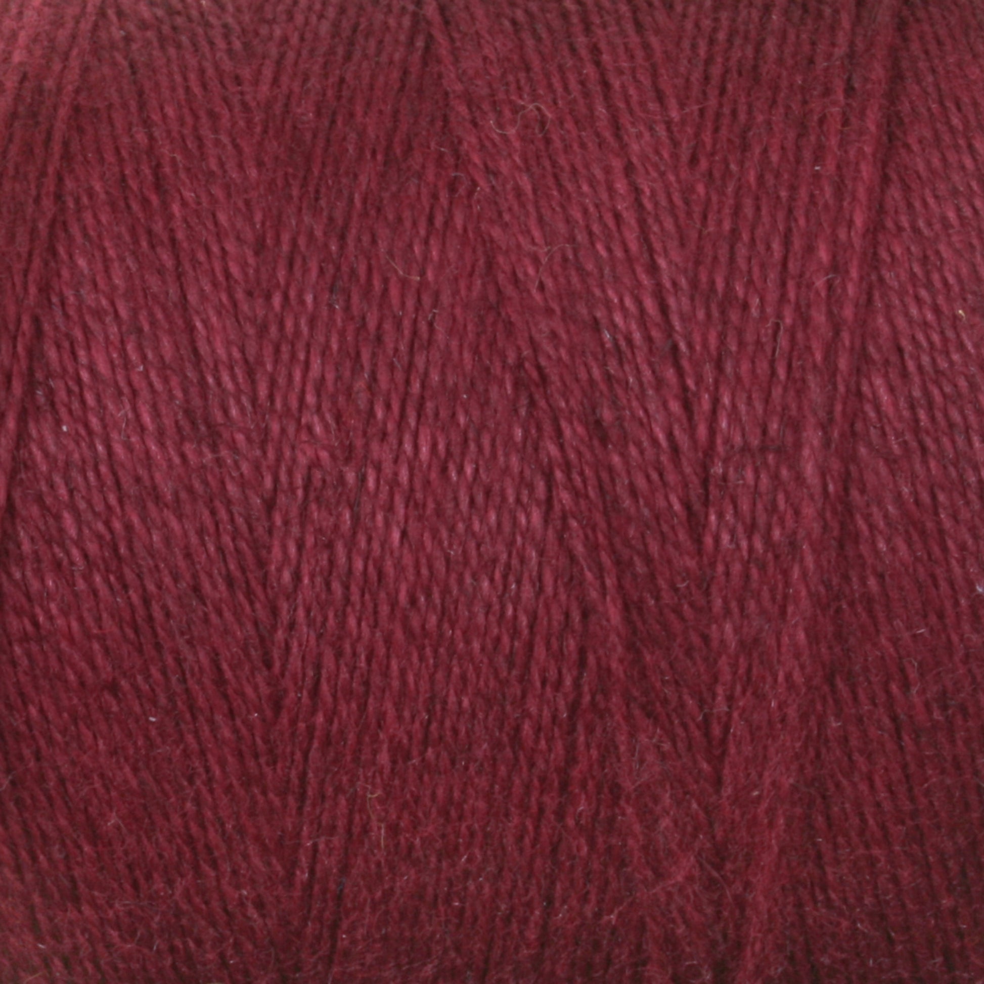 A close-up image of a spool of Maurice Brassard 8/2 Cottolin Organic Yarn in a deep, dark red hue, perfect for weaving on a four shaft loom. The texture is clearly visible, showcasing tightly wound, thin strands with a slight sheen. The rich and uniform color makes it an ideal choice for the Cottolin Tea Towel Kit.