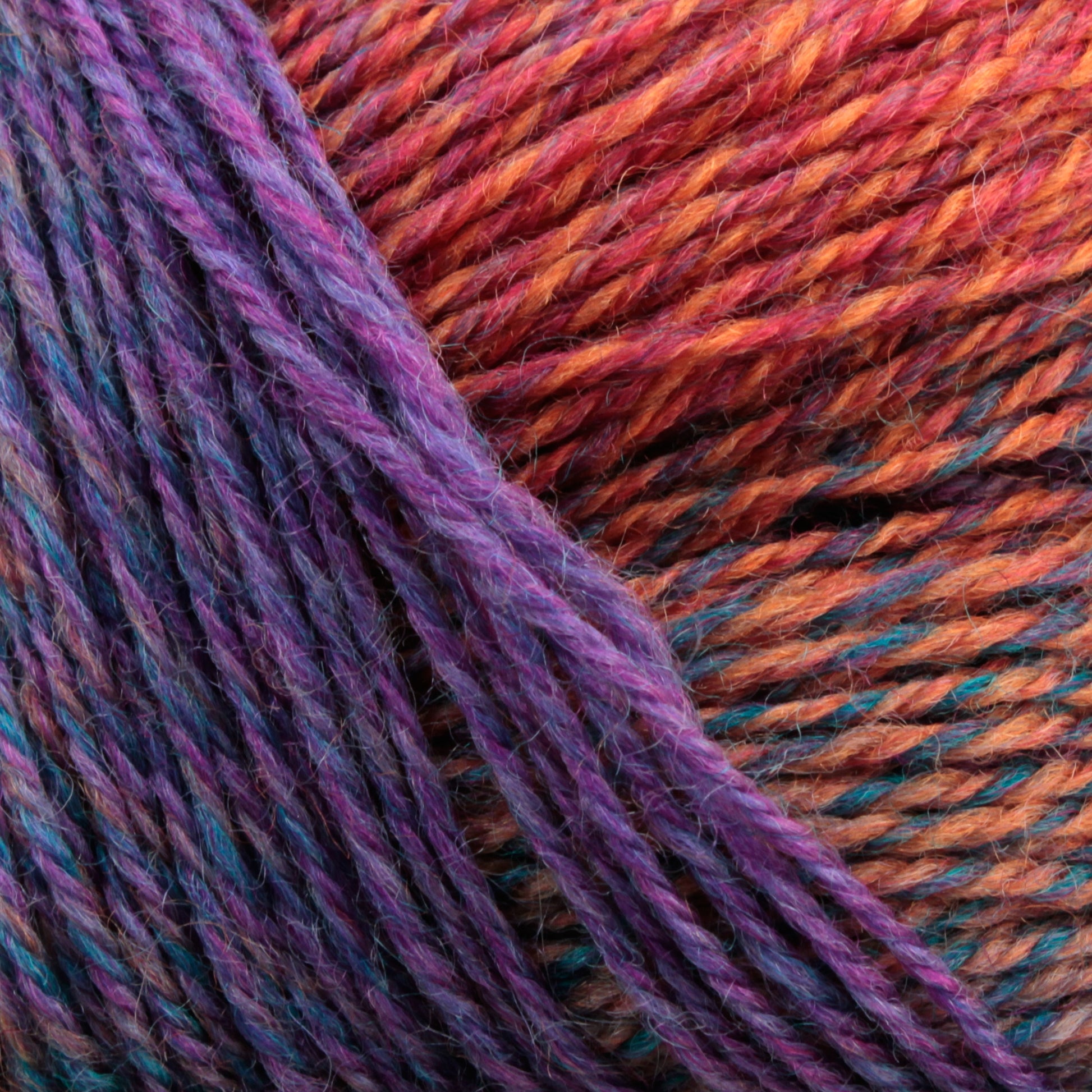 Close-up of a ball of Knitting Fever Painted Desert Yarn, showcasing a gradient pattern of purple, pink, orange, and blue. The yarn is tightly wound with visible fibers and texture, displaying the long color changes and blending of vibrant colors ideal for lightweight accessories.