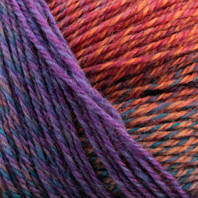 Close-up of a ball of Knitting Fever Painted Desert Yarn, showcasing a gradient pattern of purple, pink, orange, and blue. The yarn is tightly wound with visible fibers and texture, displaying the long color changes and blending of vibrant colors ideal for lightweight accessories.