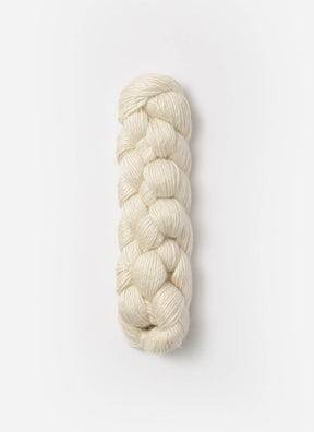 A neatly coiled hank of Blue Sky Fibers Metalico sport weight yarn is displayed against a plain white background. The off-white yarn from Blue Sky Fibers is tightly braided, showcasing its smooth texture and uniform thickness.