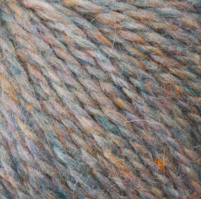 Close-up image of multicolored Peace Fleece Yarn by Harrisville Designs, highlighting grey, orange, blue, and purple threads with a soft and fuzzy texture. The wool and mohair blend fibers are intertwined, creating a thick and cozy appearance perfect for worsted weight knitting projects.