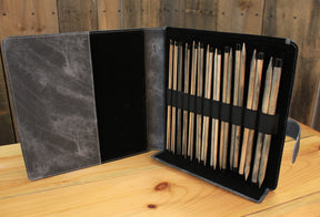 An open leather case on a wooden table holds multiple wooden-handled tools neatly organized in elastic loops. The inside flap of the case is free of tools, showcasing a soft, dark lining. The background features wooden planks. It resembles the Lykke Single-Point Knitting Needle Set, 10" by Knitting Fever / Euro Yarns, perfect for those who appreciate craftsmanship.