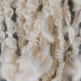 Close-up of off-white, textured Cathy - Cotton Yarn by Henry's Attic with tightly wound and curly strands, forming a visually intricate pattern. The yarn appears soft and fluffy, showcasing varying thicknesses and a slightly tangled appearance, perfect for those looking to knit or weave unique creations.