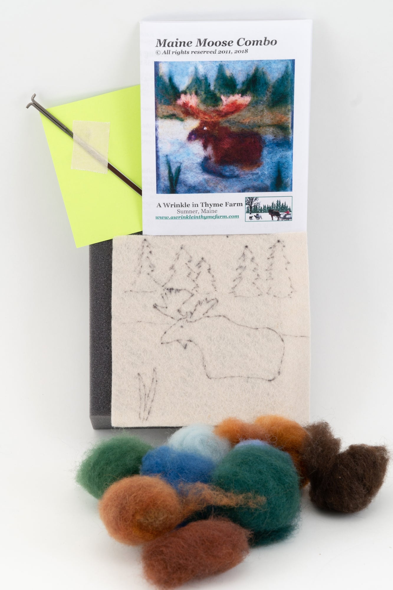 The Thyme Tile Felting Kit from A Wrinkle in Thyme Farm is displayed, featuring various colored wool roving, a sketched moose outline on fabric, a felting needle, a piece of foam, and an instructional booklet titled "Maine Moose Combo." Perfect for beginner felters, the booklet shows a completed moose project.