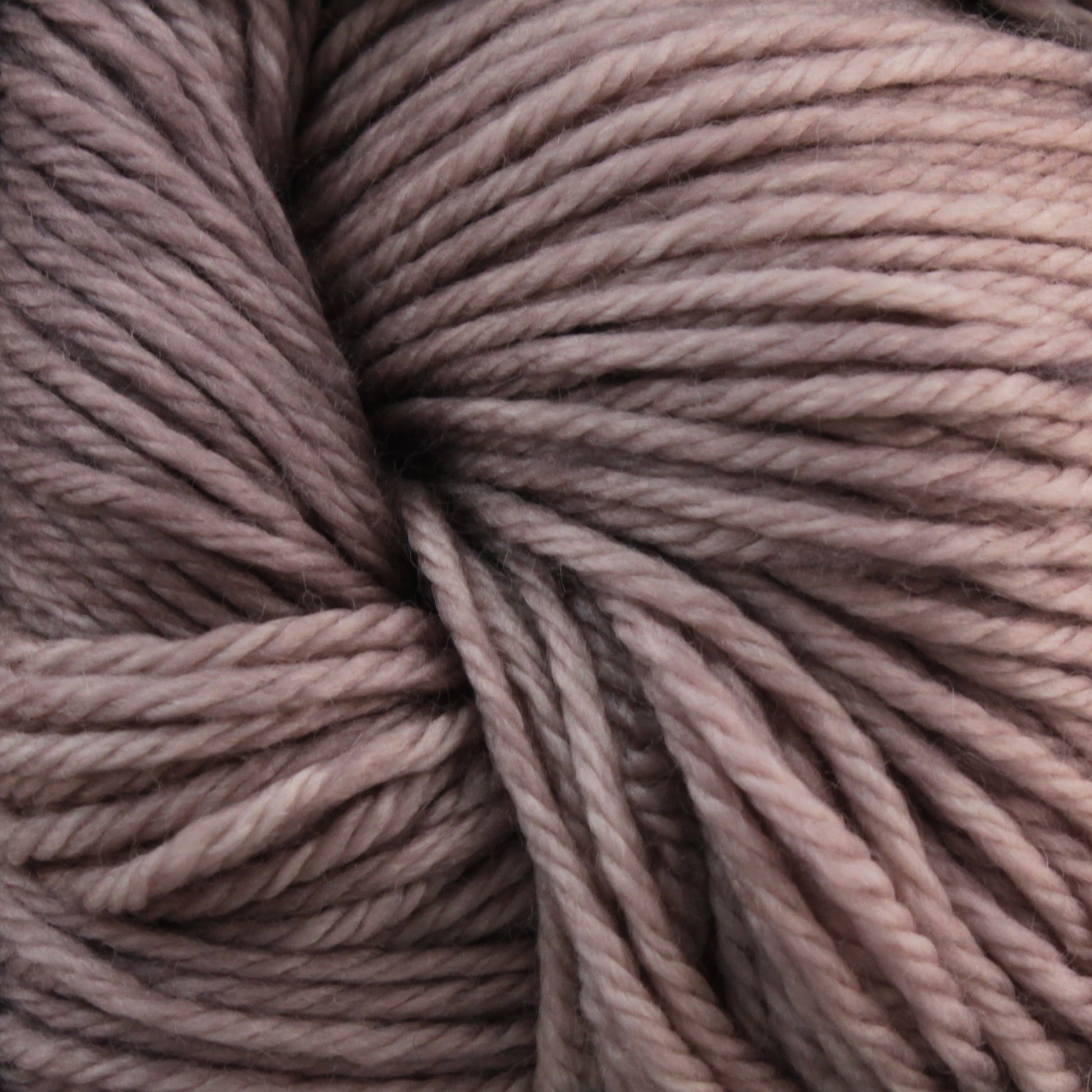 Close-up image of soft, pinkish-brown sport weight superwash merino wool yarn from Malabrigo Arroyo by Malabrigo Yarn, featuring a slightly variegated pattern. The strands are thick, twisted, and tightly wound together, creating a textured appearance perfect for crafting lightweight garments.