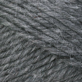 A close-up image of Lamb's Pride Bulky Yarn from Brown Sheep shows detailed textures and fibers. This gray yarn, reminiscent of Icelandic sweaters, has a slightly fuzzy appearance with strands tightly woven together, highlighting its softness and thickness.