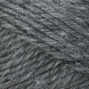 A close-up image of Lamb's Pride Bulky Yarn from Brown Sheep shows detailed textures and fibers. This gray yarn, reminiscent of Icelandic sweaters, has a slightly fuzzy appearance with strands tightly woven together, highlighting its softness and thickness.