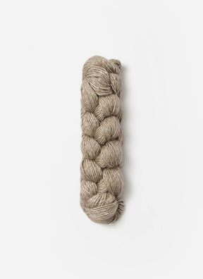 A neatly braided skein of Blue Sky Fibers Metalico sport weight yarn lies against a plain white background. The beige yarn has a subtle sheen, suggesting a smooth and potentially silky texture.