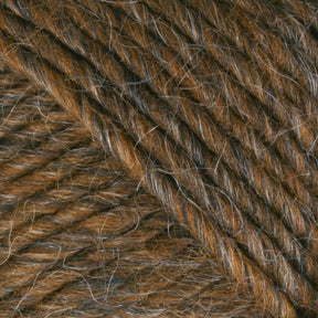 Close-up image of textured, Lamb's Pride Bulky Yarn in brown with subtle strands of gray interwoven. The fibers appear thick and soft, showcasing a rich and slightly variegated color palette. Ideal for knitters and crocheters, the image highlights the twist and intricate details perfect for creating woven blankets by Brown Sheep.