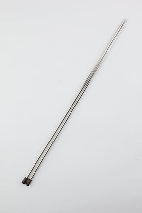 Two long, slender hollow brass pipes, part of the Accessories Unlimited Nova Platina Single Point Knitting Needles collection, are crossed over each other against a plain white background. The tips are pointed and the opposite ends have small dark-colored caps.