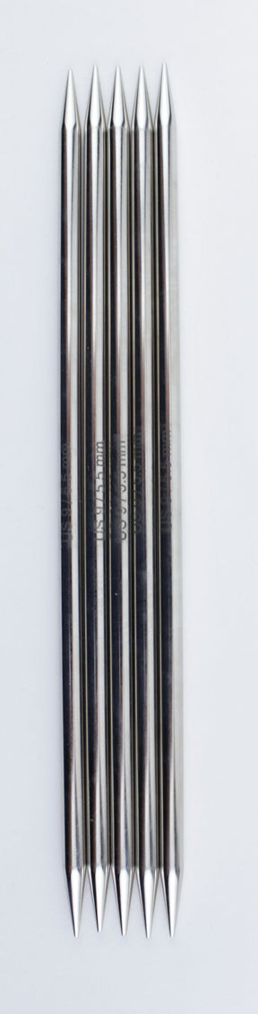 The image displays six identical, shiny, metal spike-like objects aligned vertically on a white background. Each object has a uniform cylindrical shape with tapered, pointed ends on both sides and appears polished. These high-quality chrome double-point needles are the Nova Platina Double-Point Knitting Needles from Accessories Unlimited.