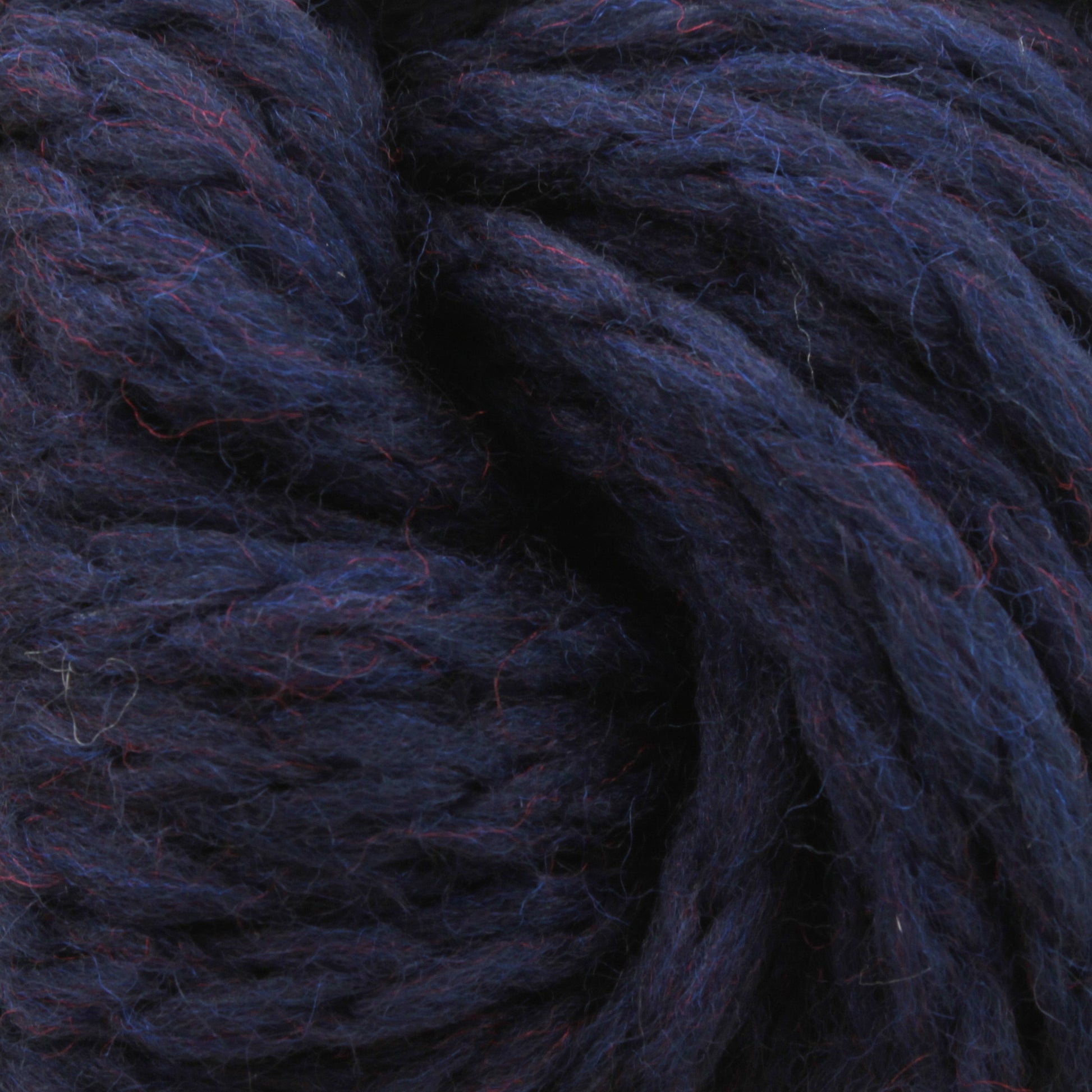 Close-up image of Ushya Yarn by Mirasol, a thick and dark blue yarn with subtle hints of other colors. The strands are tightly twisted together, revealing a textured surface with a soft and fuzzy appearance typical of the bulky weight yarn offered by Knitting Fever / Euro Yarns.