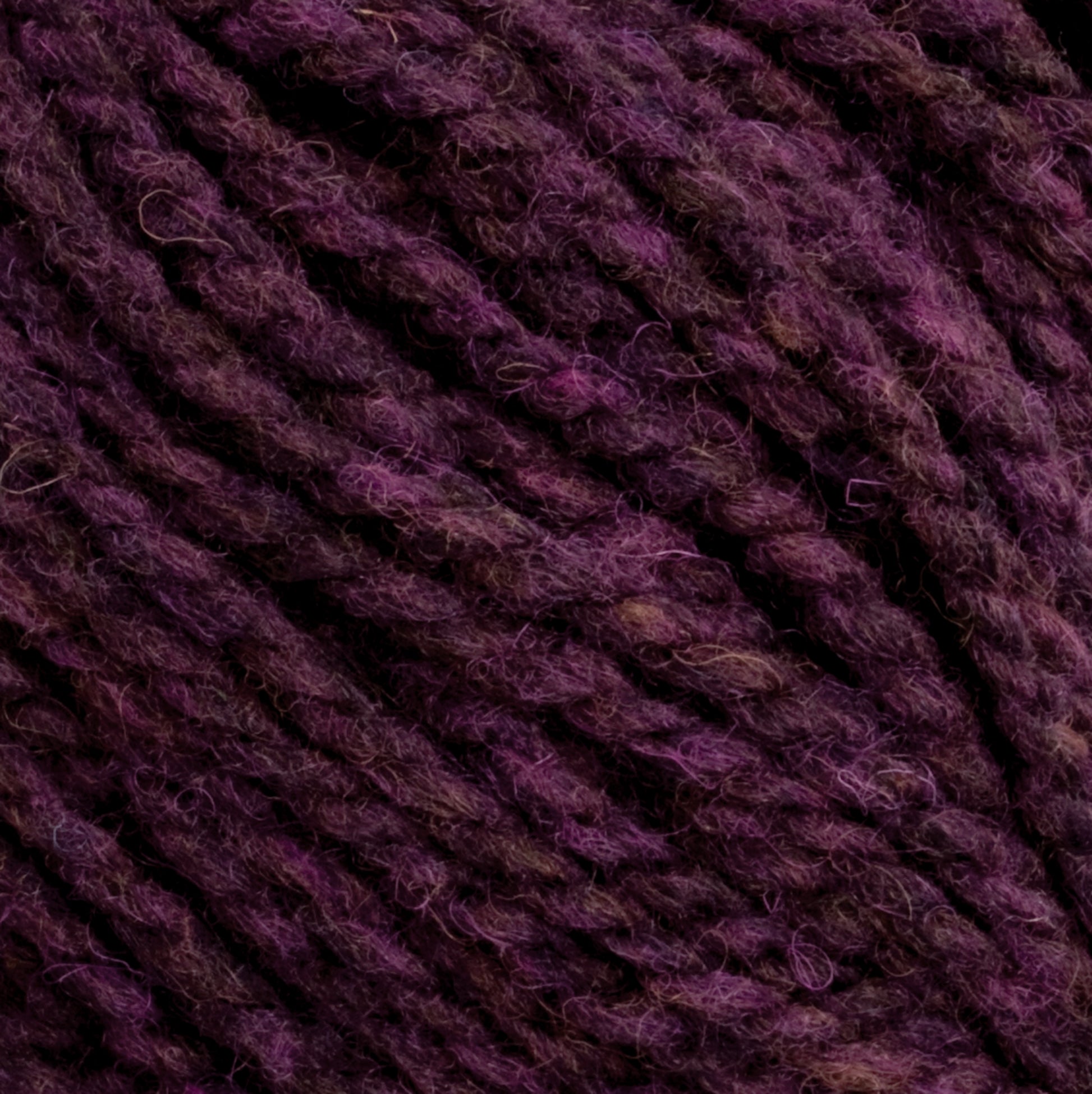 Close-up image of dark purple Harrisville Highland - Cones yarn by Harrisville Designs. The fibers are tightly twisted, exhibiting a slightly fuzzy texture. The various shades of purple create a rich, multidimensional appearance, further enhanced by the hint of spinning oils still present in this unscoured yarn.