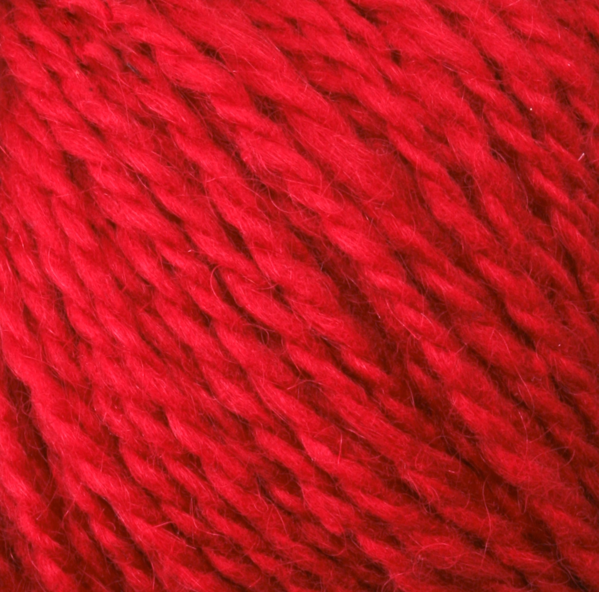 Close-up image of Harrisville Designs Peace Fleece Yarn. The texture is soft and fibrous, with multiple strands twisted together, creating a thick and uniform pattern. This wool and mohair blend displays a consistent vibrant red color throughout the yarn.