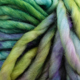 Close-up of twisted, multicolored Malabrigo Rasta wool roving featuring shades of green, yellow, blue, and purple. This soft and fluffy texture makes for super bulky yarn from Malabrigo Yarn, ideal for quick-to-knit projects. The fibers blend smoothly from one color to the next, creating an intricate and visually pleasing pattern reminiscent of the signature style of Malabrigo Rasta.