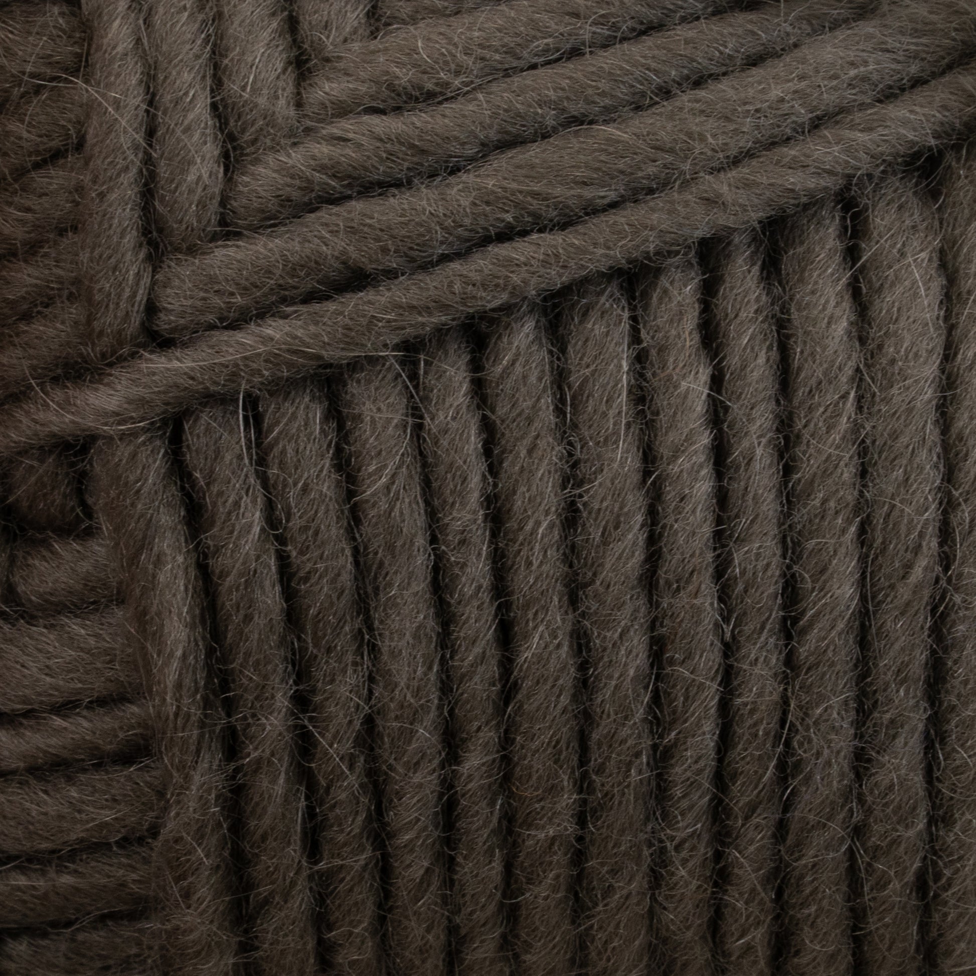 A close-up view of thick, dark gray strands of Lamb's Pride Bulky Yarn by Brown Sheep, neatly coiled together. The texture appears soft and slightly fuzzy, reminiscent of the materials used in Icelandic sweaters, with the individual fibers of each strand visible.