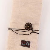 Introducing the Interchangeable Needle Case - Natural by DellaQ: a beige fabric, wallet-size case with a fold-over design, tied with a black string and secured with a large brown button. The case features numbered pockets for interchangeable set storage and has a small black label with the text "DellaQ" embroidered in light blue near the bottom.