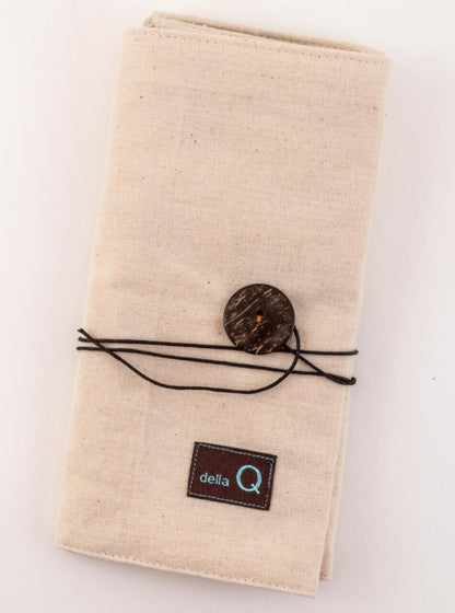 Introducing the Interchangeable Needle Case - Natural by DellaQ: a beige fabric, wallet-size case with a fold-over design, tied with a black string and secured with a large brown button. The case features numbered pockets for interchangeable set storage and has a small black label with the text "DellaQ" embroidered in light blue near the bottom.