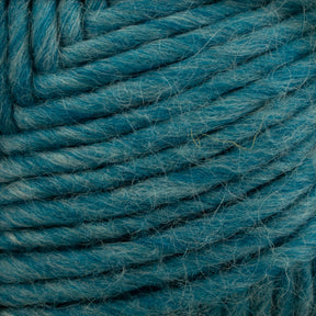 Close-up of Brown Sheep's Lamb's Pride Bulky Yarn in teal, showcasing its texture and fibers tightly wound into a ball. The strands appear soft and slightly fuzzy, with varying shades of teal creating a marbled effect perfect for knitters and crocheters dreaming up their next Icelandic sweaters.