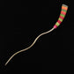 The Striped Color Stick Shawl Pin by Bonnie Bishoff Designs, created by Bonnie Bishoff, is a wavy S-shaped metal knitting needle featuring a vibrant polymer clay handle adorned with horizontal stripes of red, orange, yellow, green, and pink against a black background. The needle's tip is pointed.