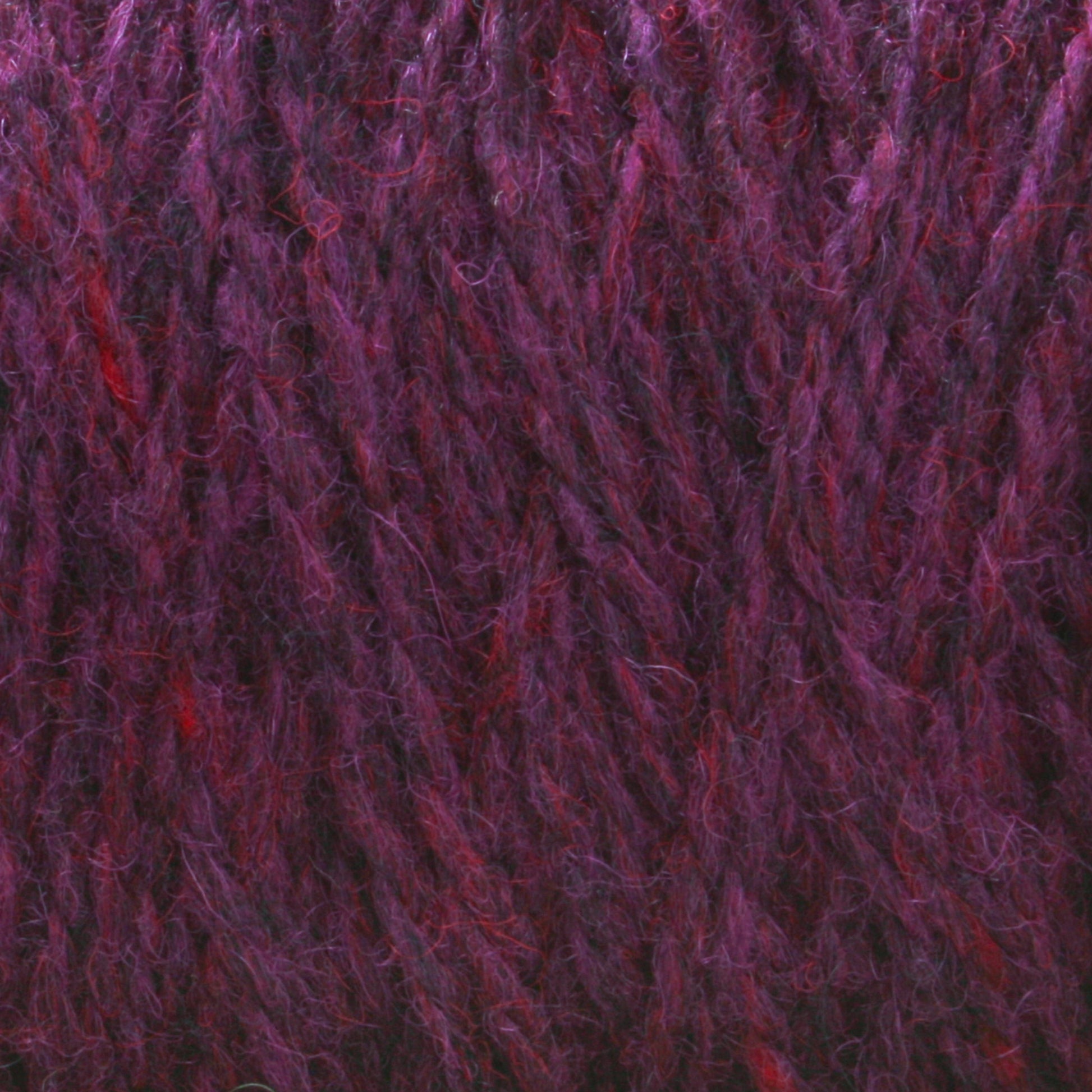 A close-up shot of purple and red variegated Harrisville Highland - Cones yarn from Harrisville Designs showcases its soft, fuzzy texture with interwoven strands creating a rich, multi-tonal appearance. Traces of spinning oils are still visible.