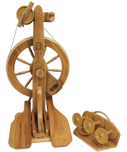 The Majacraft Rose Spinning Wheel, crafted by Majacraft Co., boasts a high-speed whorl and includes a set of four additional wooden bobbins. The traditional double-treadle design features an intricate carved pattern on the main upright support, and the bobbins are neatly arranged on a matching wooden holder.