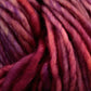 Close-up image of thick, multi-colored Malabrigo Mecha yarn in shades of red, purple, and pink. The kettle-dyed fibers from Malabrigo Yarn are twisted and slightly fuzzy, forming a textured, intertwined pattern.