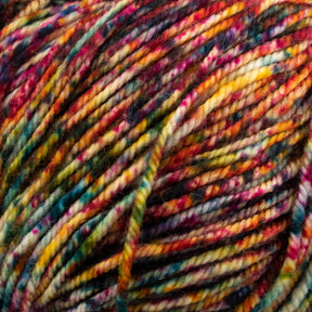 A close-up image of the Malabrigo Yarn's Malabrigo Sock kettle dyed multicolored yarn displays a variety of vibrant hues including red, yellow, green, blue, and purple. The superwash merino wool yarn appears soft and thick, with intricate color blending creating a rich and textured visual effect.