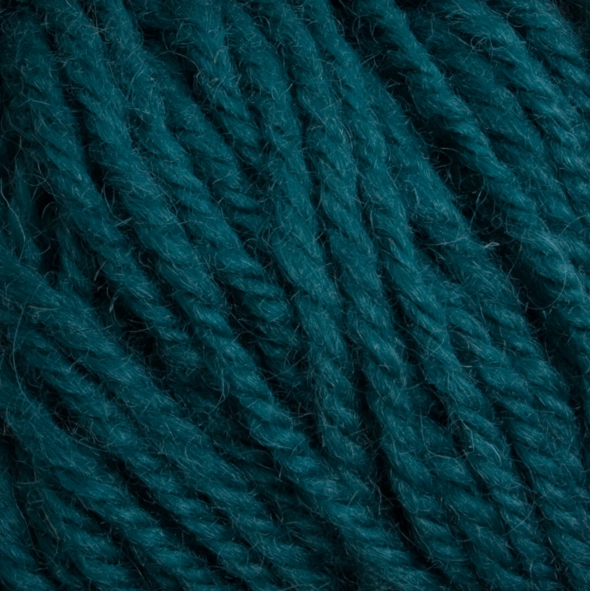 Close-up photo of Halcyon Deco Rug Wool by Caledonian Dye Works, revealing the texture and detail of individual dark teal strands twisted together. Lint and fibers highlight the cozy warmth of this versatile yarn, perfect for any project.