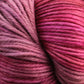 A close-up view of a ball of yarn featuring various shades of pink and maroon. The smooth-textured Malabrigo Arroyo by Malabrigo Yarn, made from sport weight superwash merino wool, is tightly wound, showcasing the intricate details of the strands and color transitions, making it perfect for crafting lightweight garments.