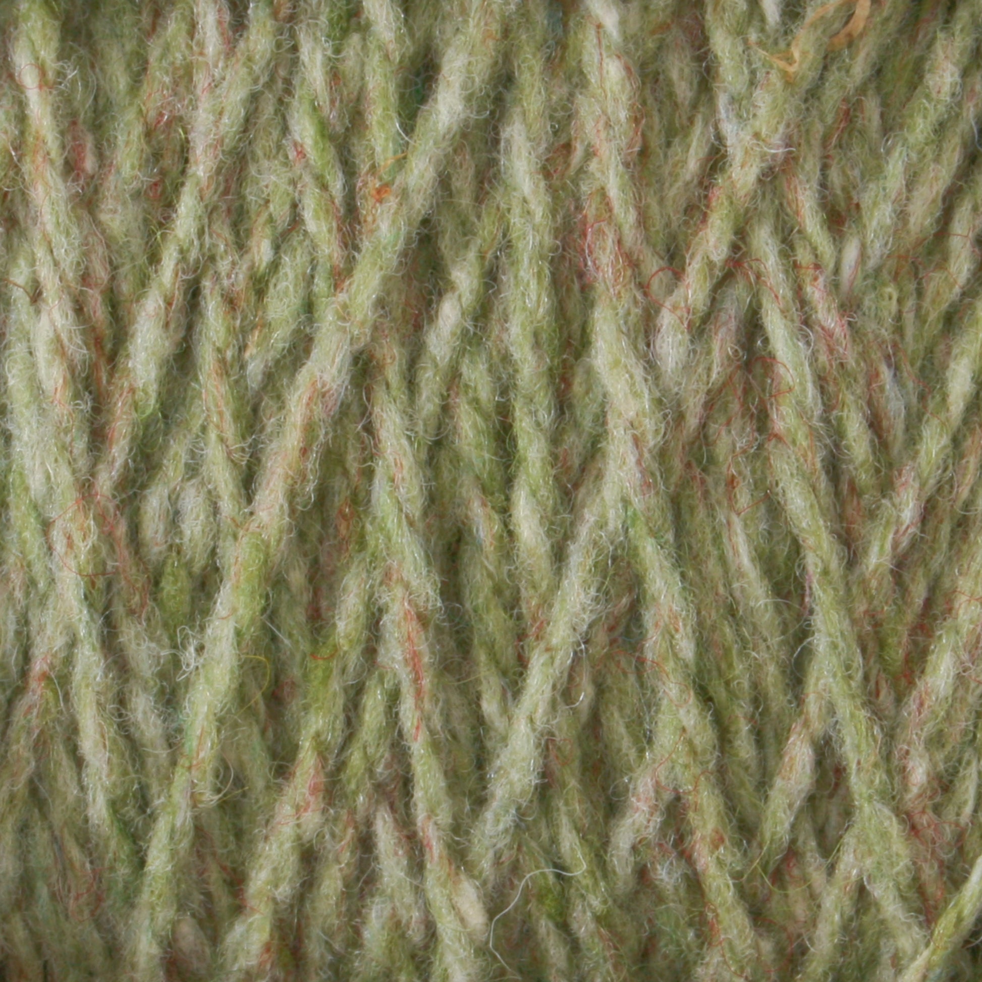 Close-up image of green Harrisville Designs Harrisville Highland - Cones yarn with a blend of orange and beige fibers intertwined. The texture appears soft and fluffy, showcasing the detailed strands of this unscoured yarn.