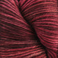 Close-up of a skein of sport weight superwash merino wool yarn from Malabrigo Yarn's Malabrigo Arroyo, showcasing a spectrum of red shades from deep crimson to lighter pinks. The texture reveals intricate twists and slight fuzziness, making it ideal for lightweight garments with a soft, tactile appearance.