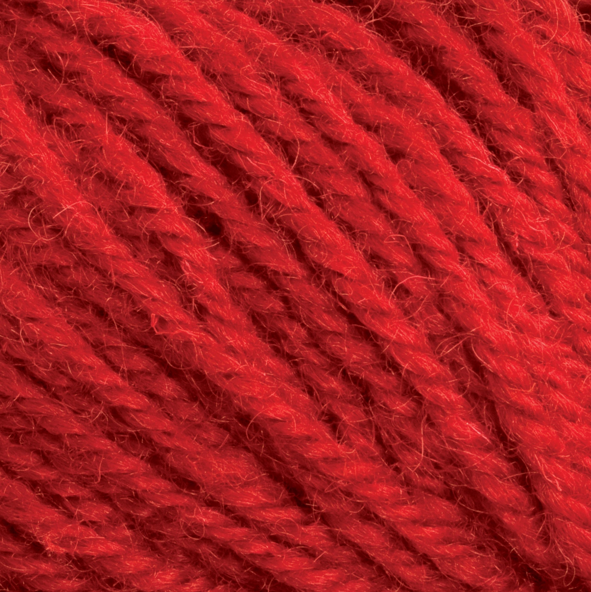 Close-up of Halcyon Deco Rug Wool from Caledonian Dye Works showing detailed fibers and texture. The thick, twisted strands come together to form a rich, vibrant red color. The image highlights the softness and quality of this 100% wool yarn, making it suitable for knitting or crochet projects. Perfect for creating a luxurious deco rug yarn piece.