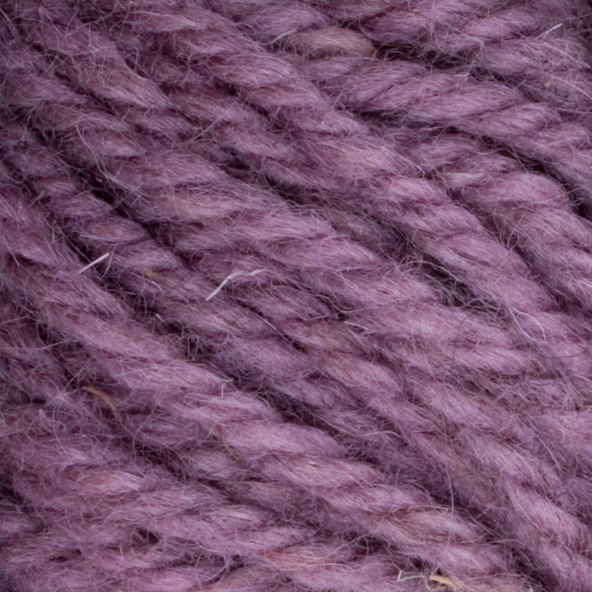 Close-up of soft purple yarn fibers. The texture shows tightly spun strands with slight fuzz, indicating Halcyon Yarn Classic Rug Wool by Caledonian Dye Works, a wool blend material favored by rug weavers. The consistent color, enhanced by hand-dye techniques, showcases nuanced variations in the fibers for an artisanal touch.